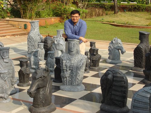 A person in a blue shirt sits atop large chess pieces.